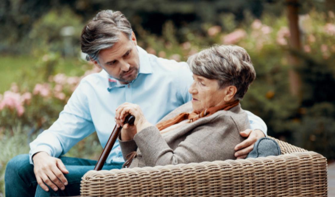 Man supporting elderly woman with stick sitting on chair