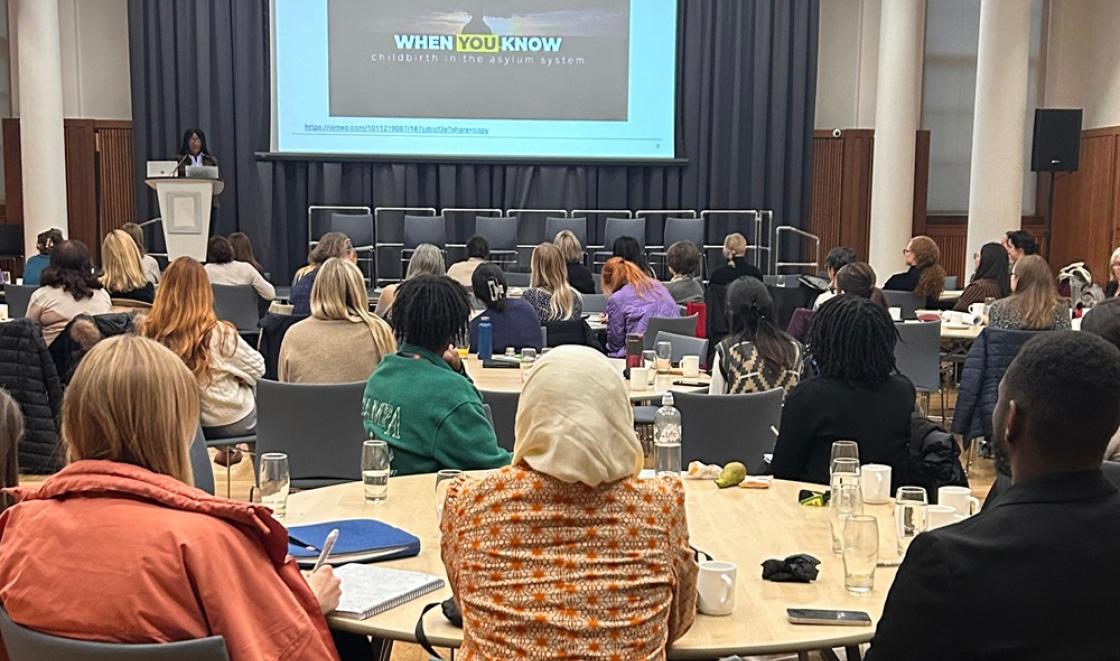 A group of people sitting at a table watching a presentation at the conference