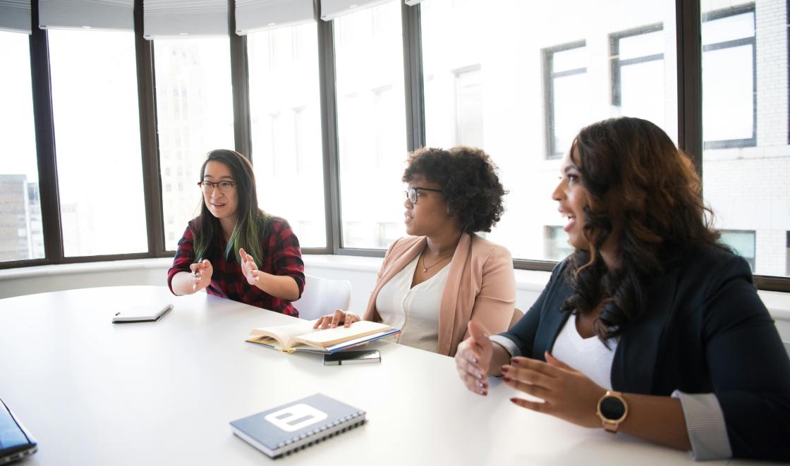 Three women sit at table having a discussion in a patient and public involvement group