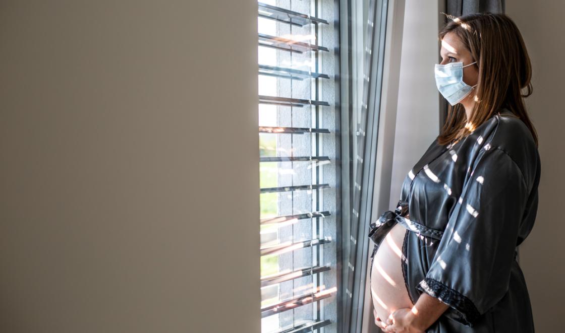 Pregnant woman with mask looking out of hospital window