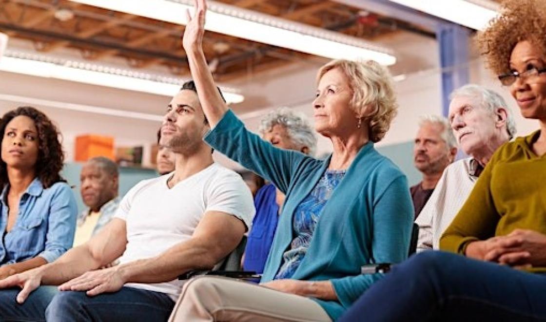 Woman with her hand up in the audience of a public meeting