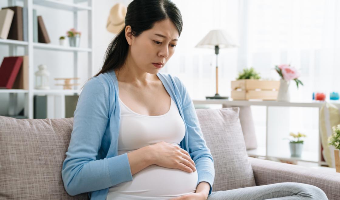 Worried pregnant woman sitting on sofa